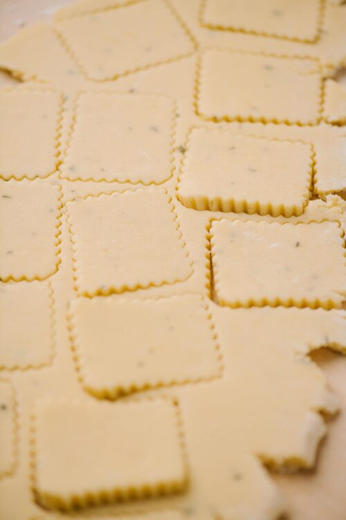 Butter cookie dough cut into squares with scalloped edges.