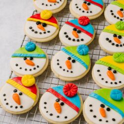 Colorful snowman decorated cookies for winter holiday baking on a wire rack.