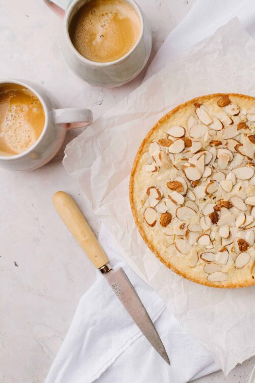 Fresh almond cake with toasted almonds and two cups of coffee on white background.