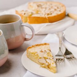 Butter almond cake slice on white plate with forks and coffee cups.