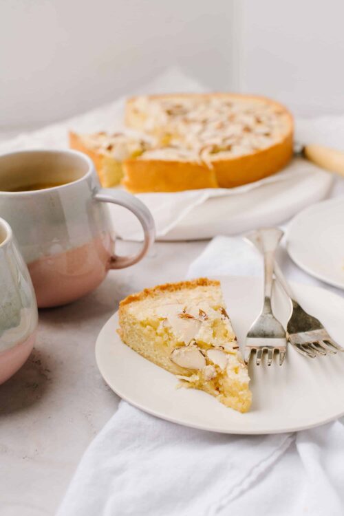 Butter almond cake slice on white plate with forks and coffee cups.