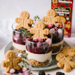 Gingerbread cookies and layered berry cheesecake parfaits on a tray, perfect for holiday desserts.