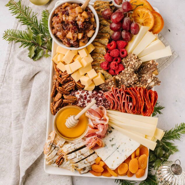 Cheese and charcuterie board with fresh fruits, nuts, honey, and holiday decorations for festive occasions.