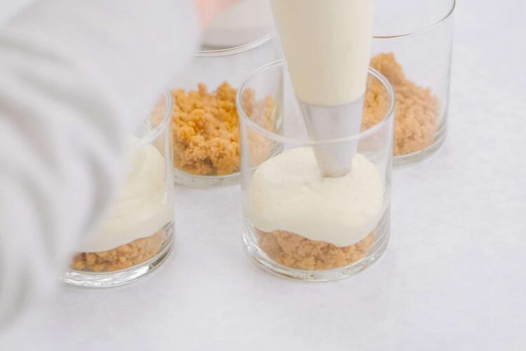 Creamy dessert being layered with graham cracker crumbs in glass cups.