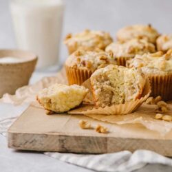 Buttery walnut muffins with crumbly tops on a wooden board, served with a glass of milk and a bowl of salt.