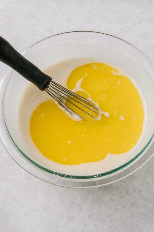 Freshly prepared yellow cake batter in a glass mixing bowl with a whisk.