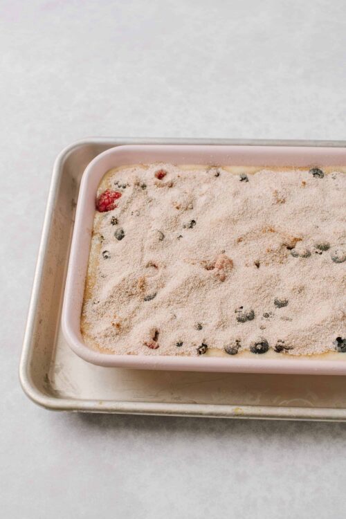 Fresh berry cobbler before baking in a pink ceramic dish.