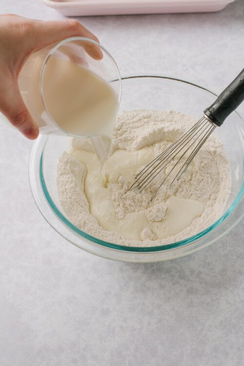 Cream being poured into a mixing bowl with flour and a whisk during baking.
