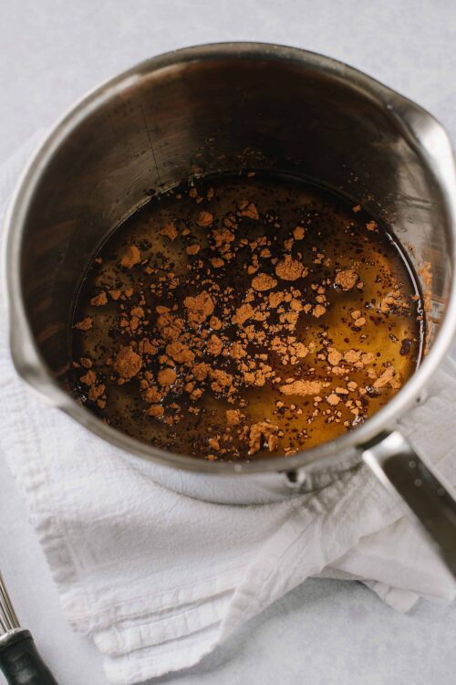 Aromatic spices and vanilla bean soaking in hot syrup in a stainless steel pot.
