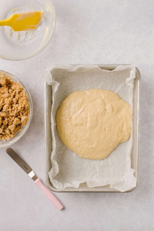 Buttery cookie dough on baking sheet with crumbly streusel and mixing bowl with spatula in background.