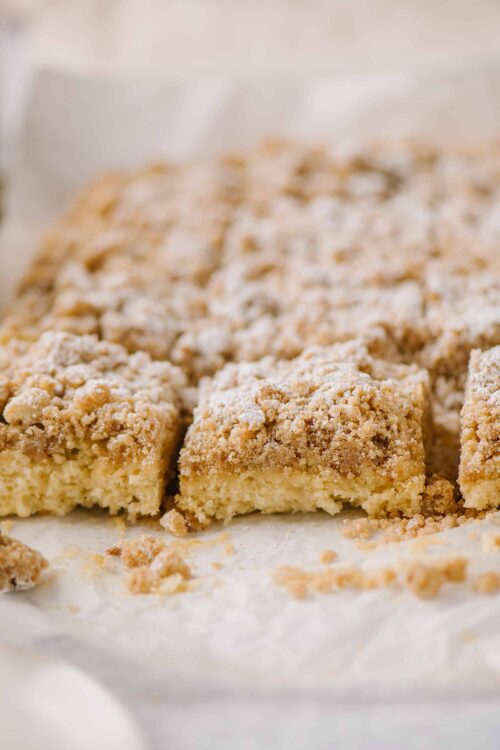 Buttery crumb-topped coffee cake with streusel and vanilla glaze on white parchment.
