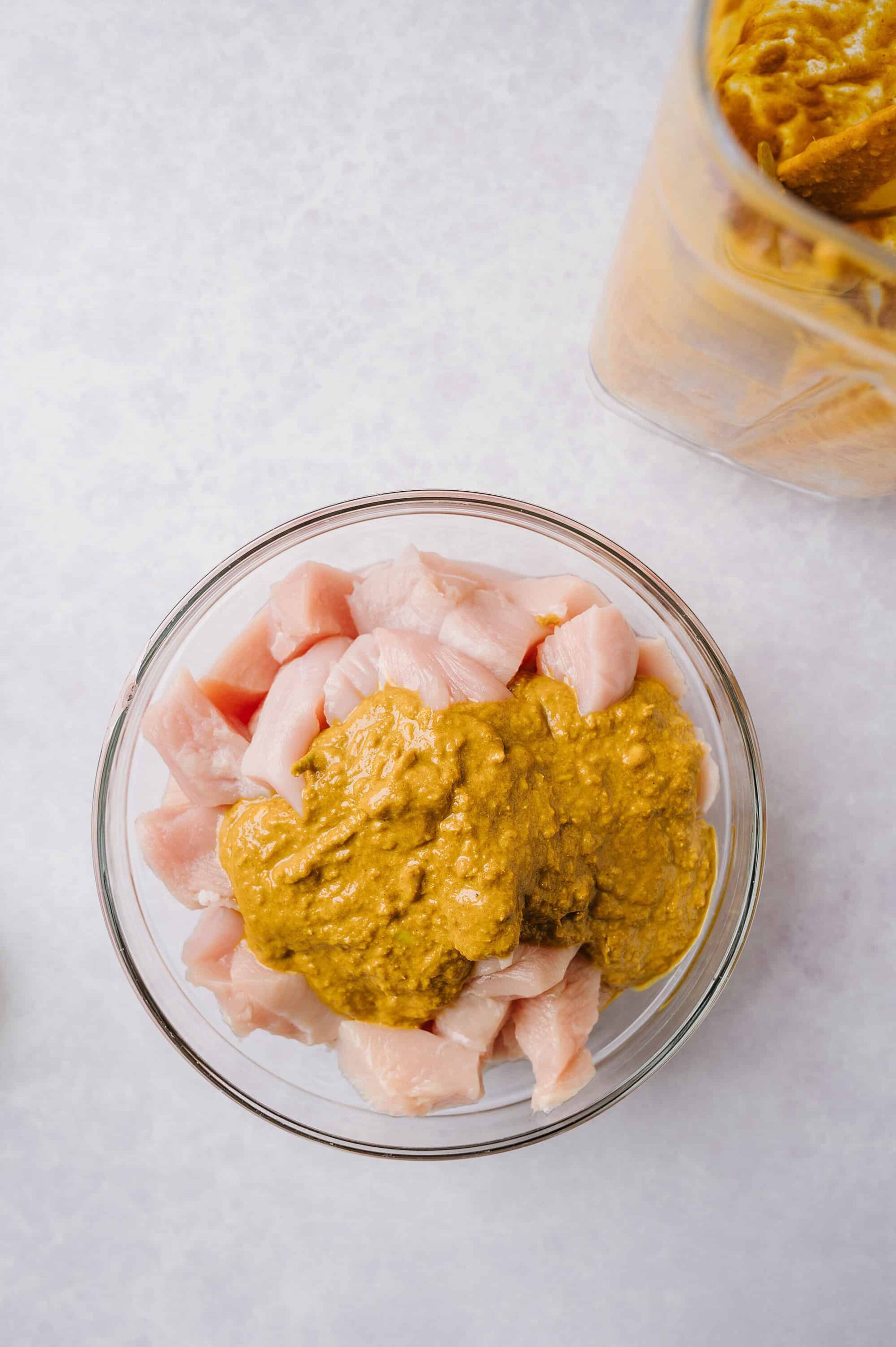 Raw chicken pieces with mustard sauce in a glass bowl, prep for baking or cooking.