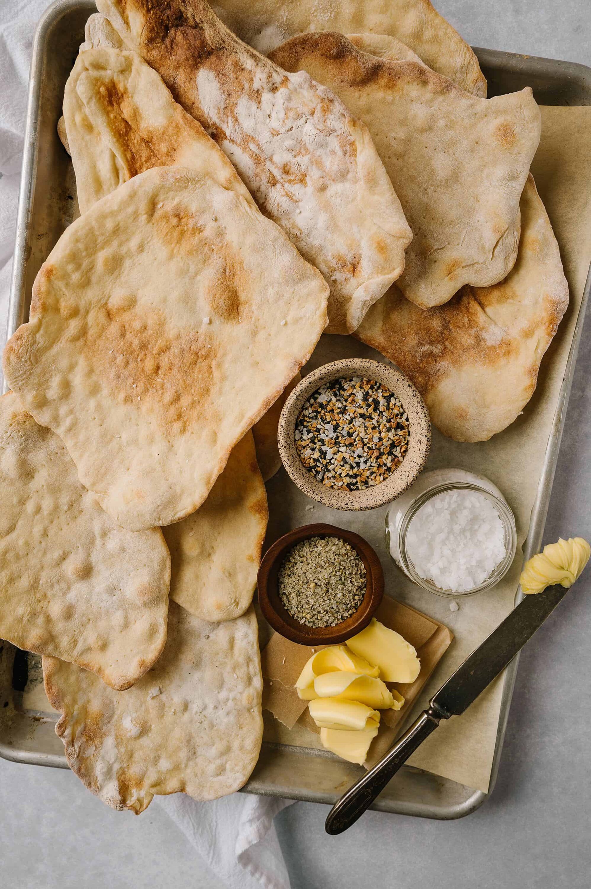 Fluffy homemade flatbreads with butter, spices, and seasonings on a baking sheet. Perfect for pizza, wraps, or dipping.