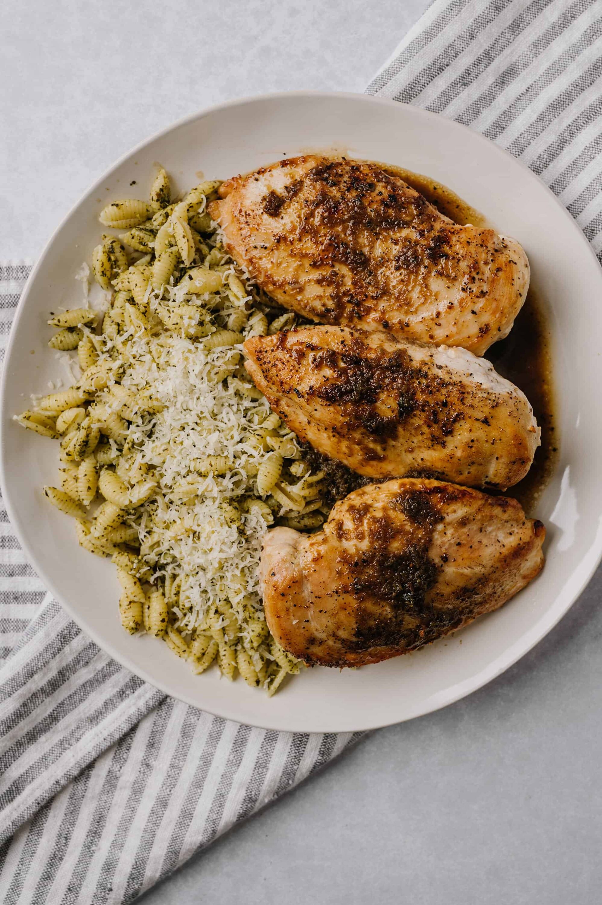 Roasted chicken thighs with herb pasta and grated cheese on white plate.