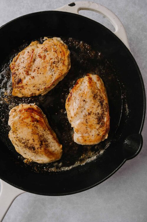 Juicy pan-seared chicken breasts cooking in a black skillet with crispy, seasoned exterior. Perfect for easy dinner recipes.