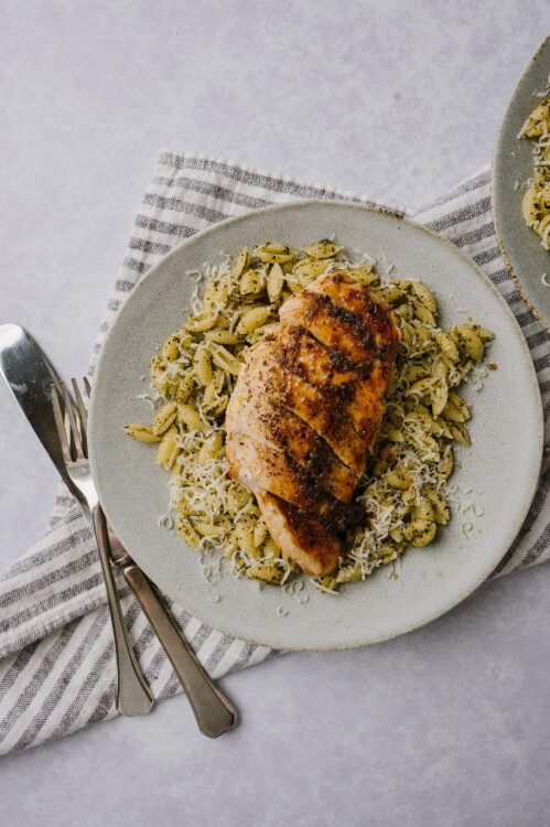 Succulent roasted chicken breast with pesto fusilli pasta on white plate.