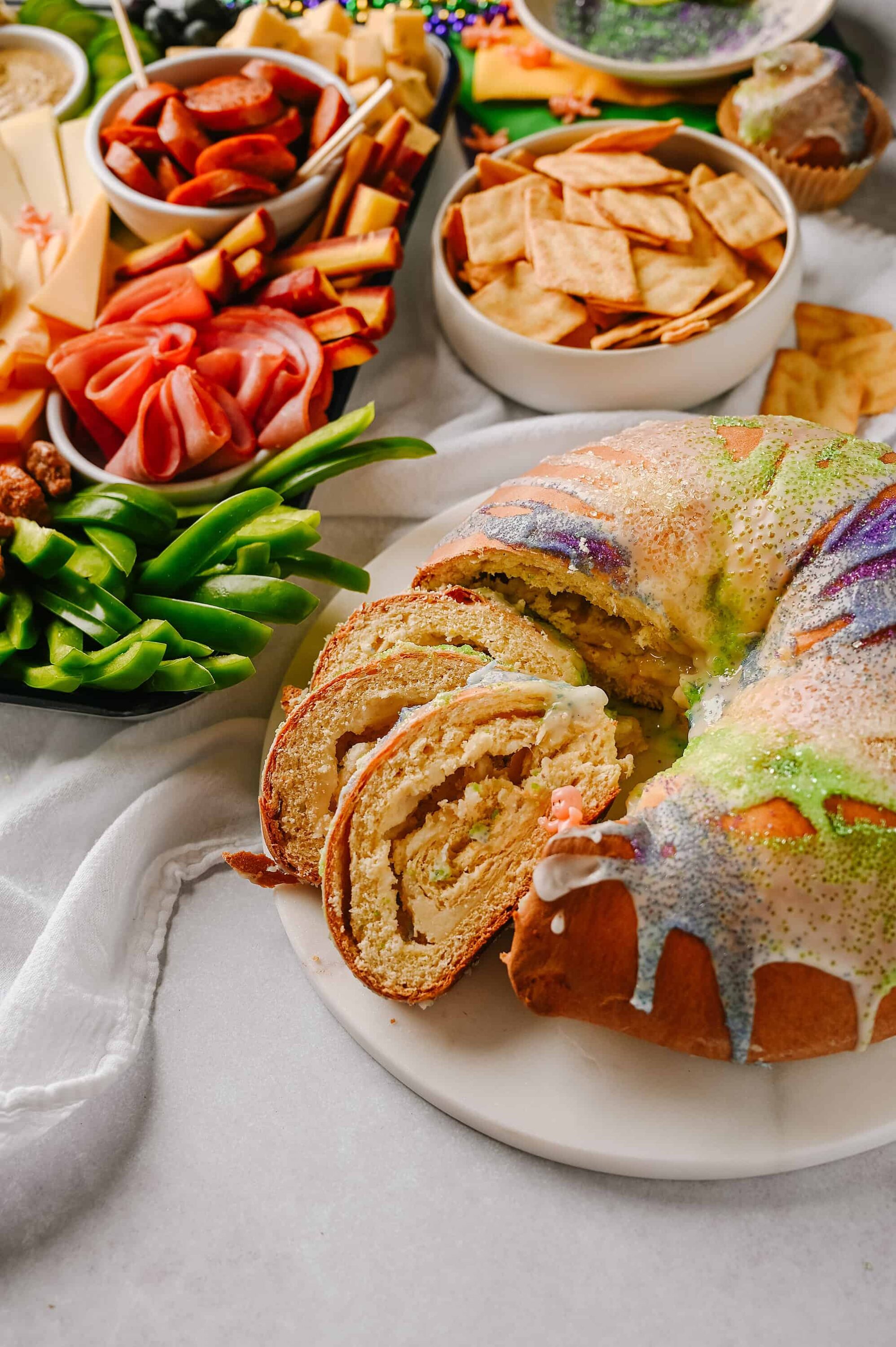 Colorful birthday cake with rainbow sprinkles and sliced pieces on a white plate, surrounded by holiday snack platters and fresh vegetables.
