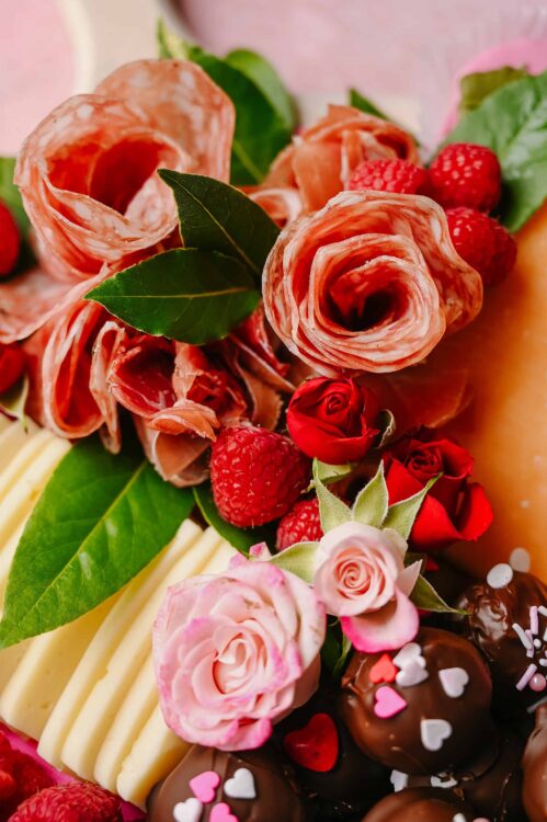 Fresh charcuterie with cured meats, berries, roses, and chocolates - perfect for romantic celebrations.