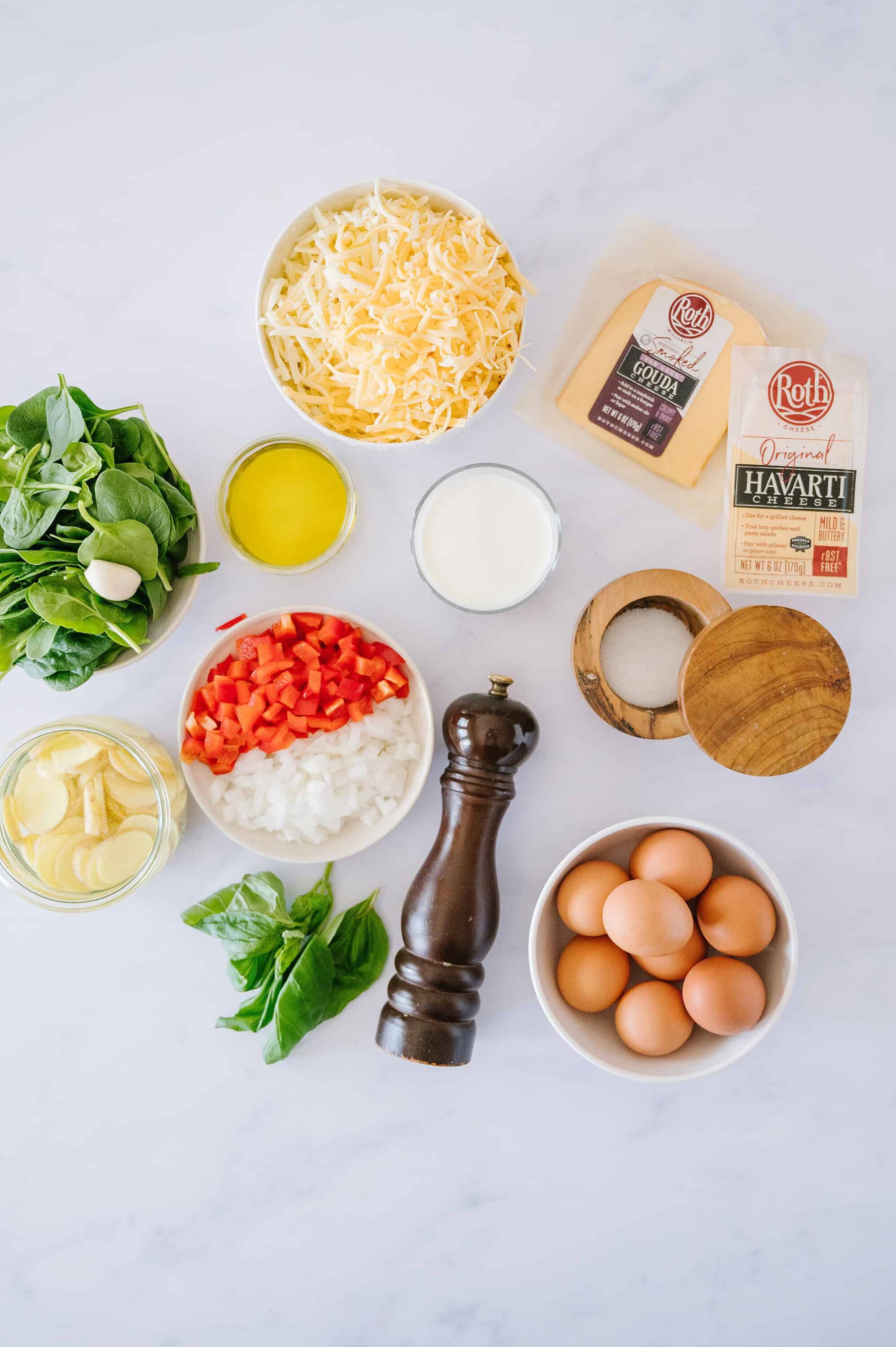 Shredded cheese, milk, eggs, chopped vegetables, and herbs for a cheesy egg casserole recipe.