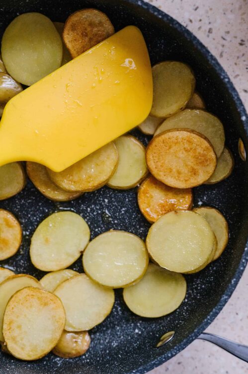 Golden roasted potato slices with melting butter in a black skillet, ready for cooking.