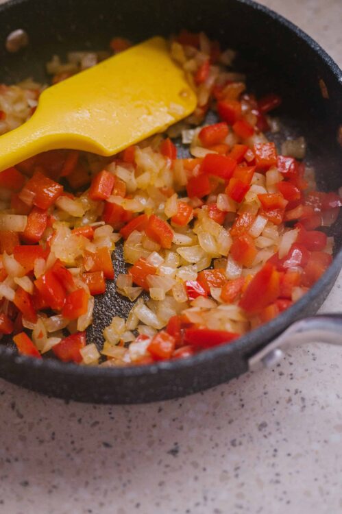Diced onions and red bell peppers cooking in a black skillet.