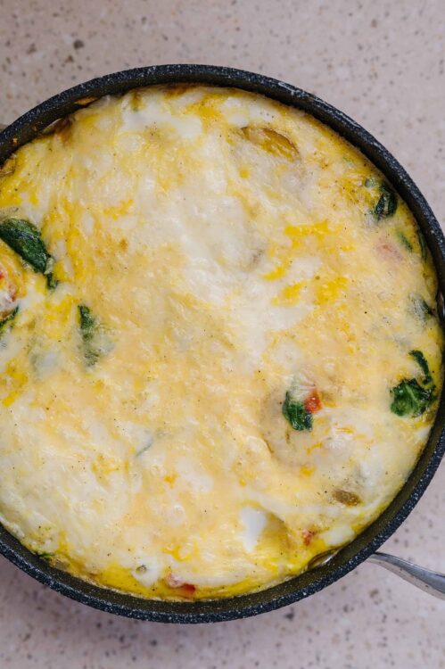 Creamy scrambled eggs in a black skillet with herbs and vegetables, perfect for breakfast or brunch.