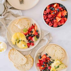 Fluffy scrambled eggs with fresh berries and bread on white plates.