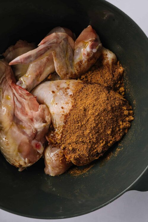 Seasoned raw chicken with spices and herbs in a black skillet for baking or cooking.