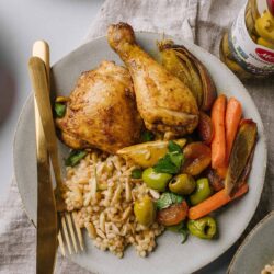 Roasted chicken with Mediterranean vegetables and orzo pasta on a ceramic plate.