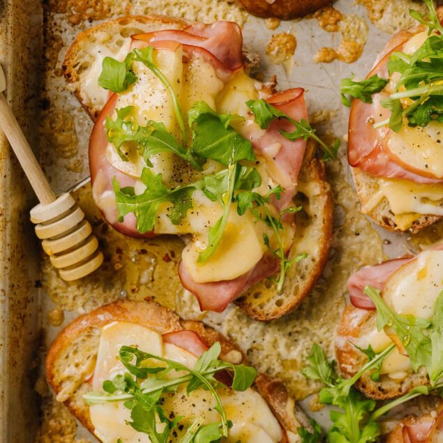Savory open-faced sandwiches with ham, cheese, and greens on toasted bread.