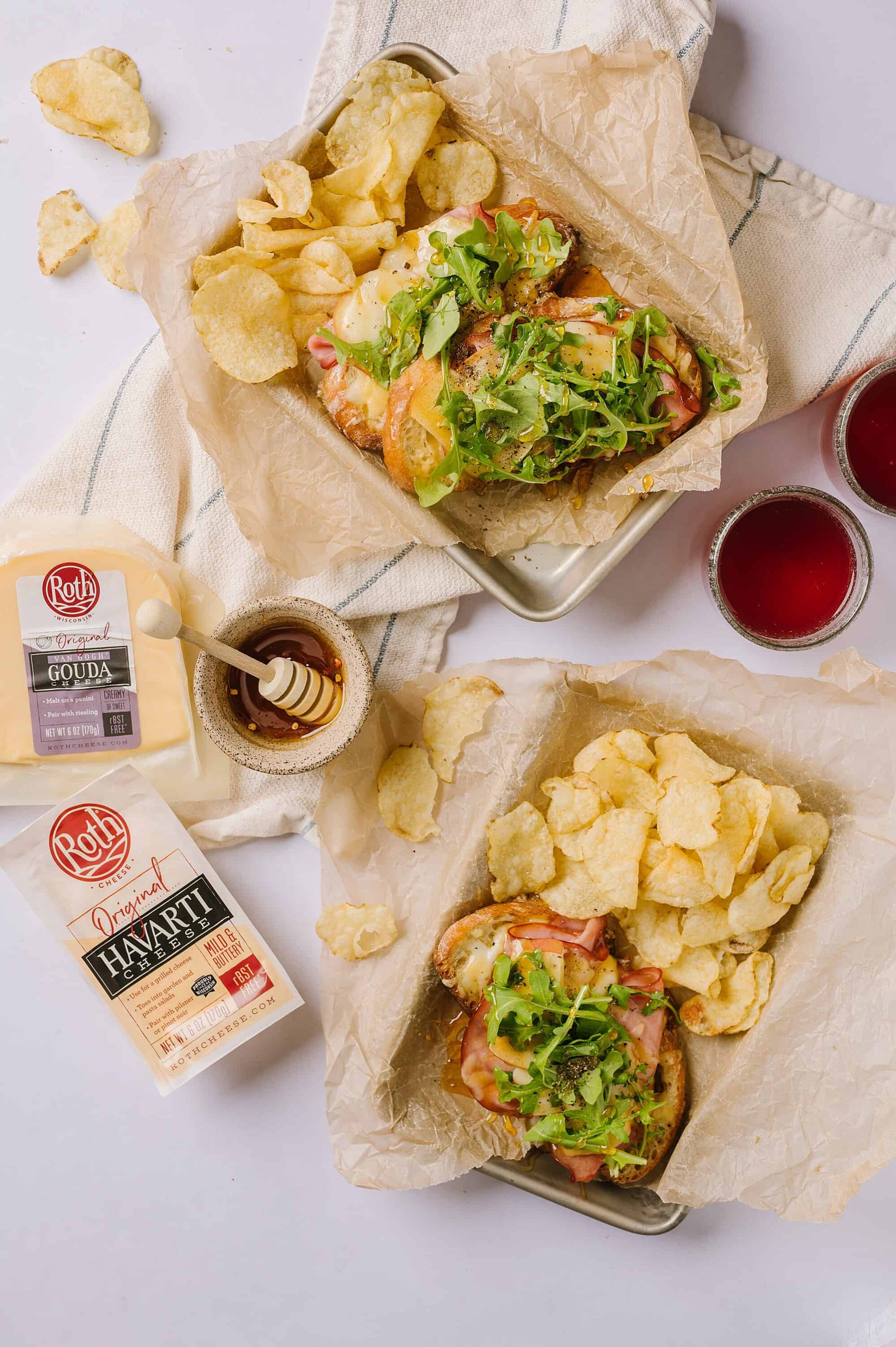 Golden potato chips and gourmet sandwiches with melted cheese, ham, and fresh greens.
