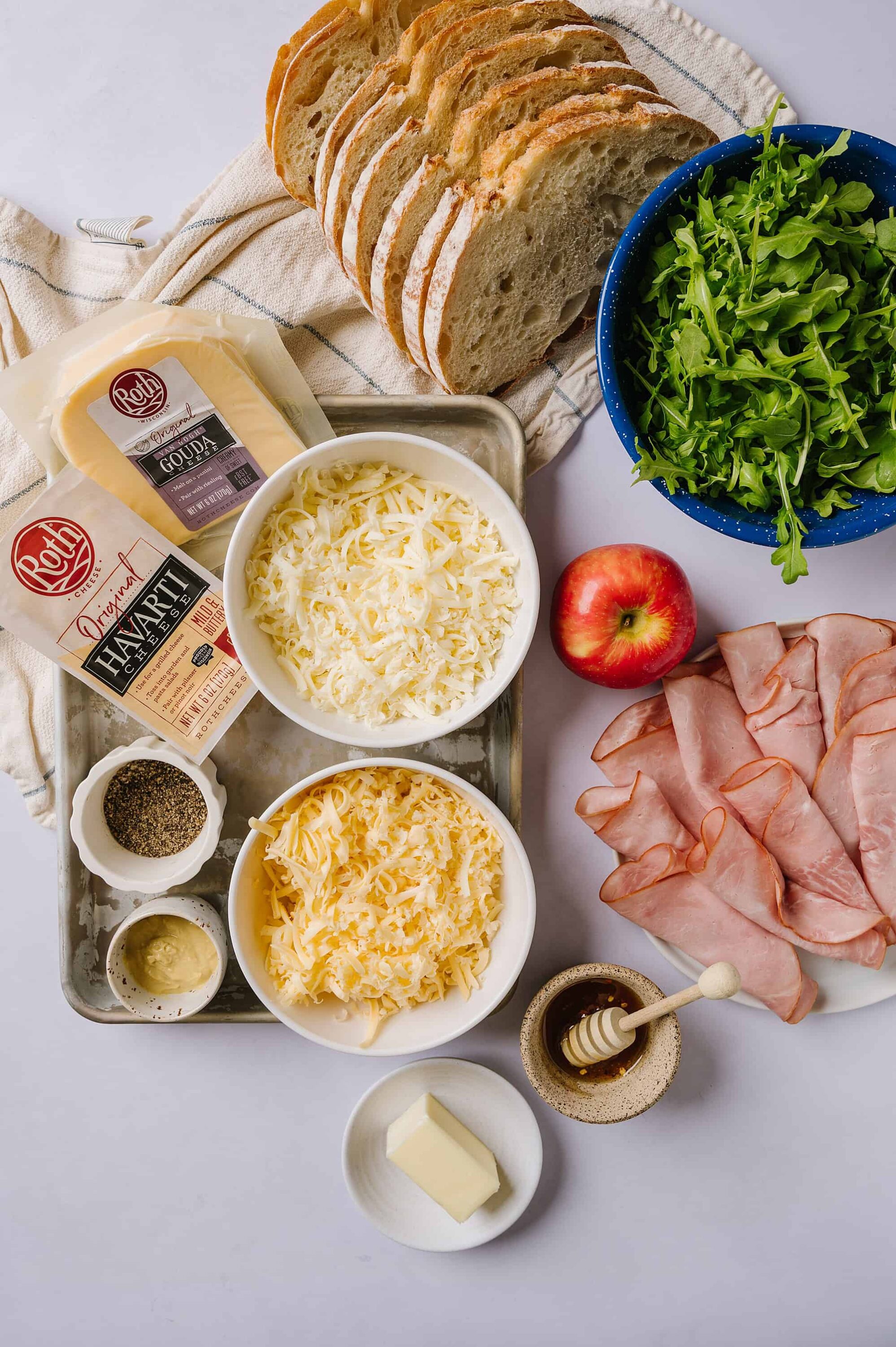 Sliced rustic bread, cheese, and deli meats for a delicious sandwich preparation. Fresh greens, apple, and condiments ready to assemble sandwiches.