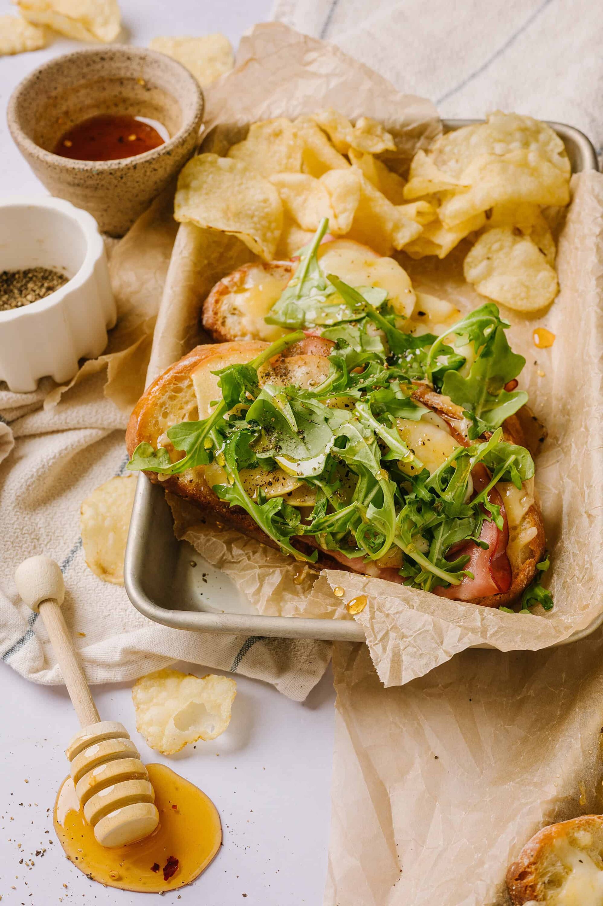 Crispy bacon sandwich with fresh greens and roasted potatoes on baking sheet.