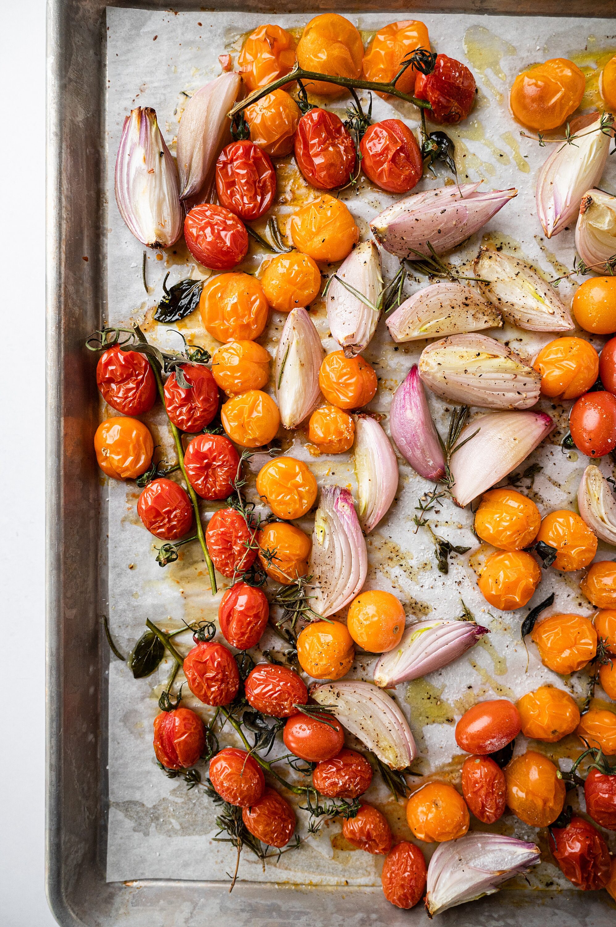 Roasted cherry tomatoes and garlic on baking sheet for flavorful vegetable dish.