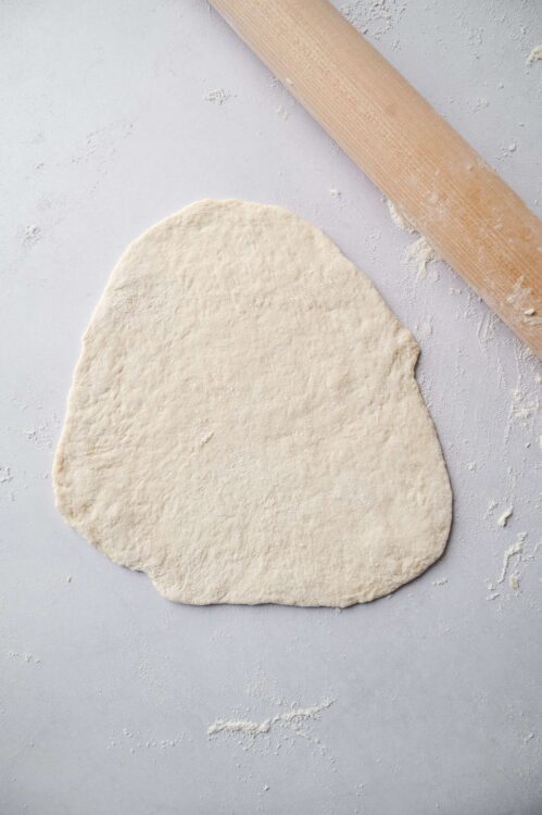 Dough rolled out on a floured surface with a rolling pin in the background.