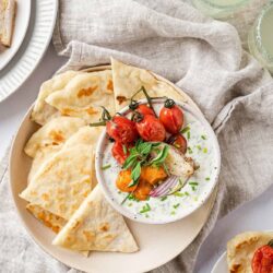 Fresh Greek tzatziki with cherry tomatoes, pita bread, and cucumber on a rustic linen cloth.