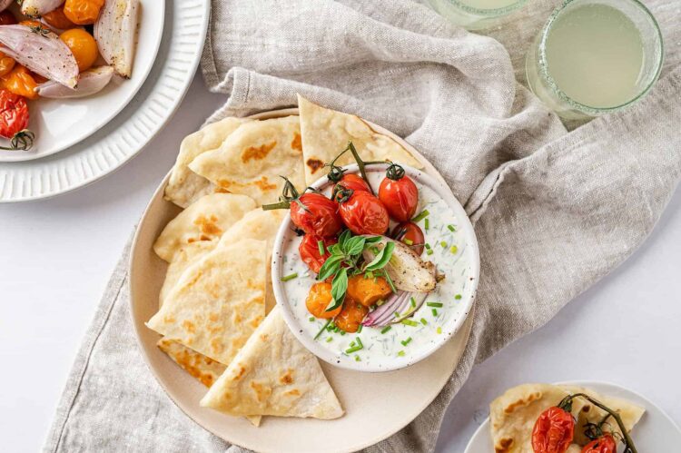 Fresh Greek tzatziki with cherry tomatoes, pita bread, and cucumber on a rustic linen cloth.