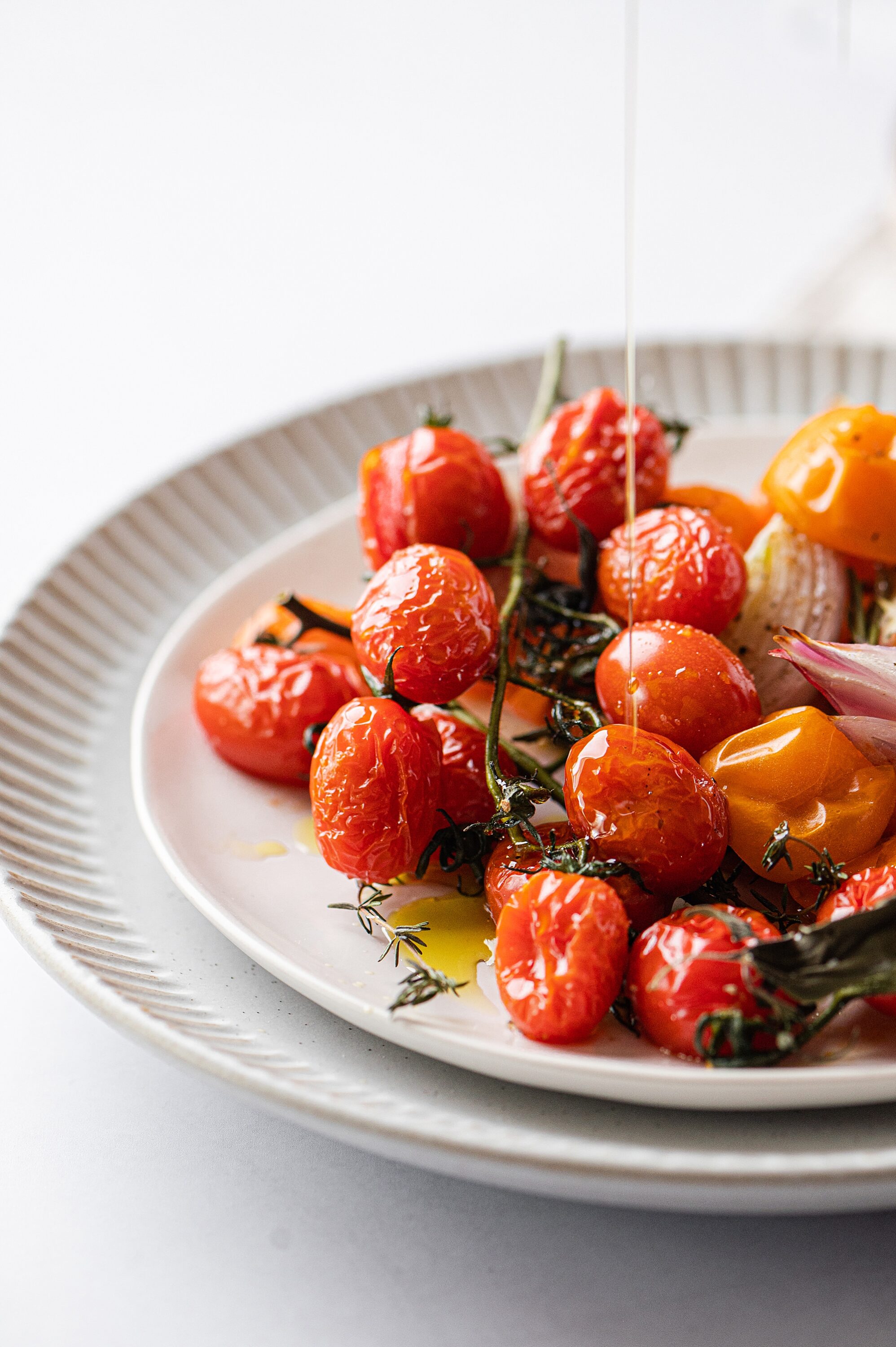 Fresh roasted cherry tomatoes with herbs and olive oil on a white plate.