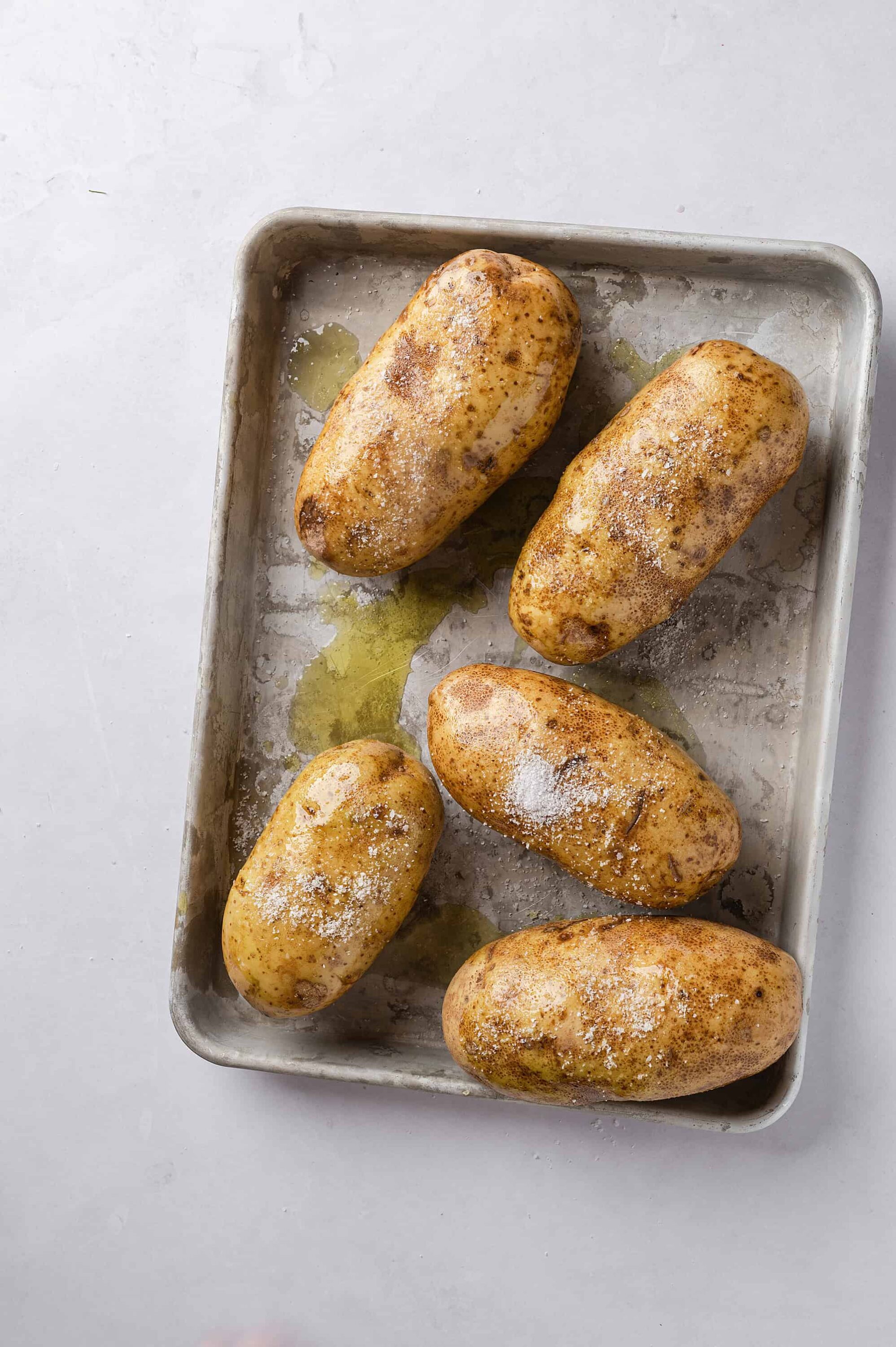 Baked potatoes seasoned with salt and olive oil on a baking sheet.
