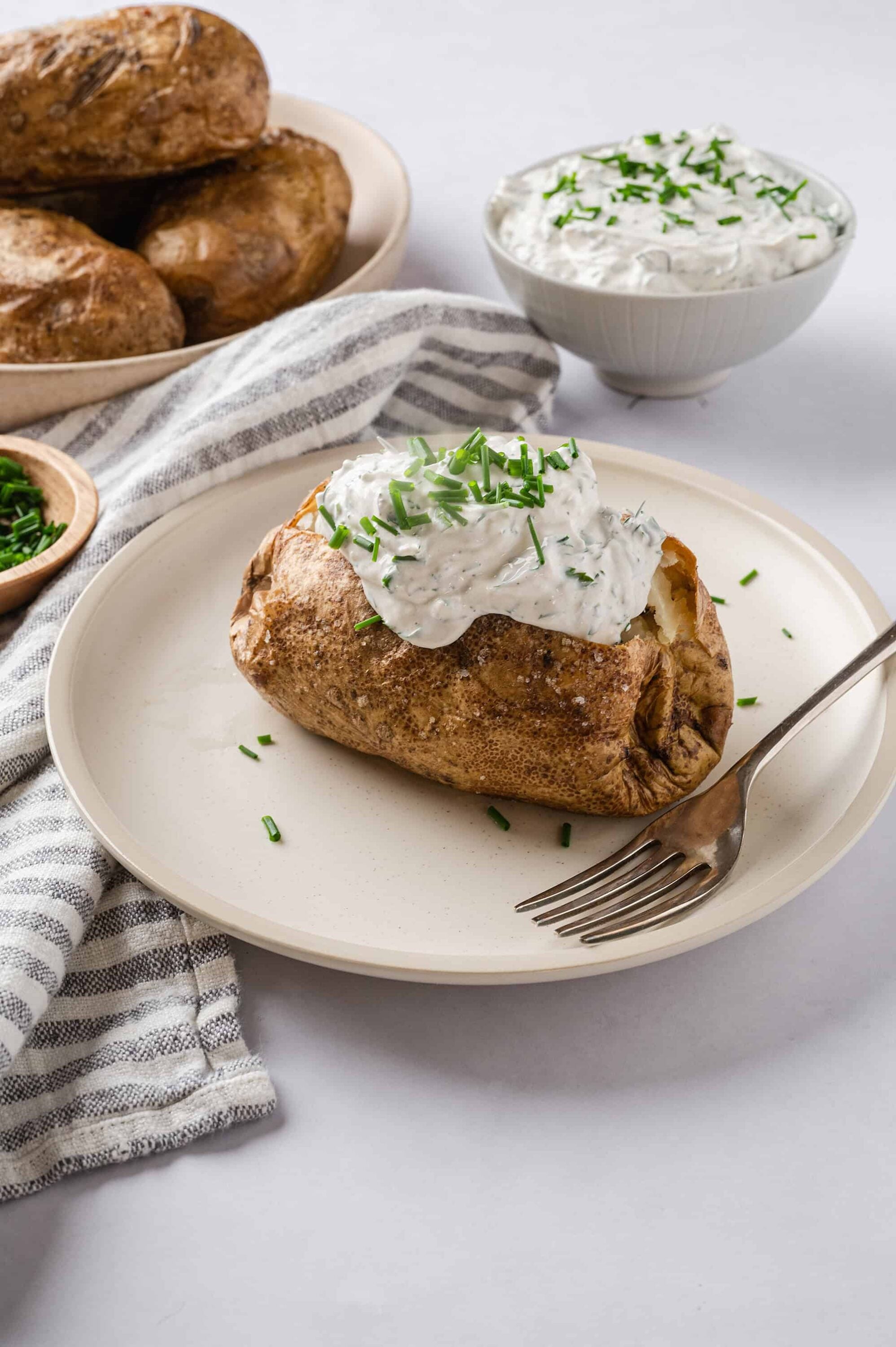 Baked potato with creamy herb sour cream topping on a neutral plate.
