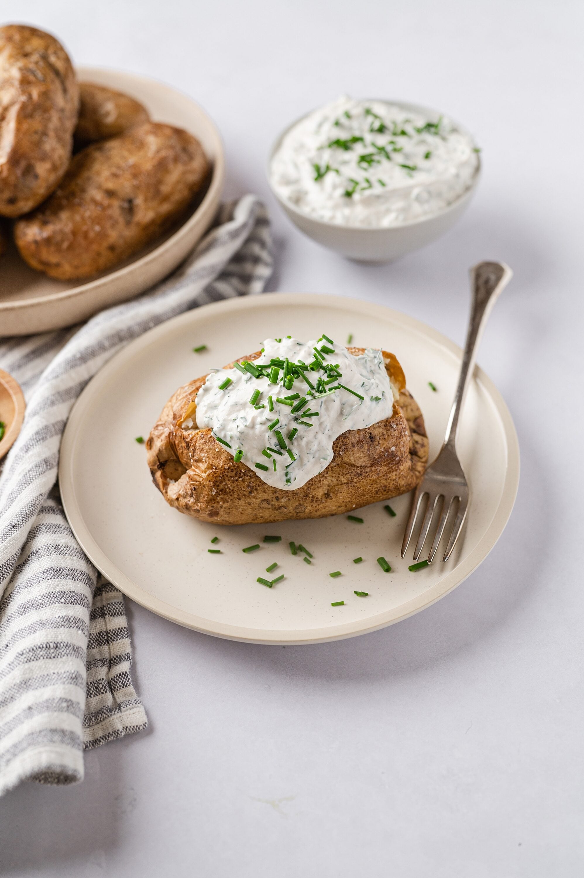 Creamy baked potato with chive sour cream topping on white plate.