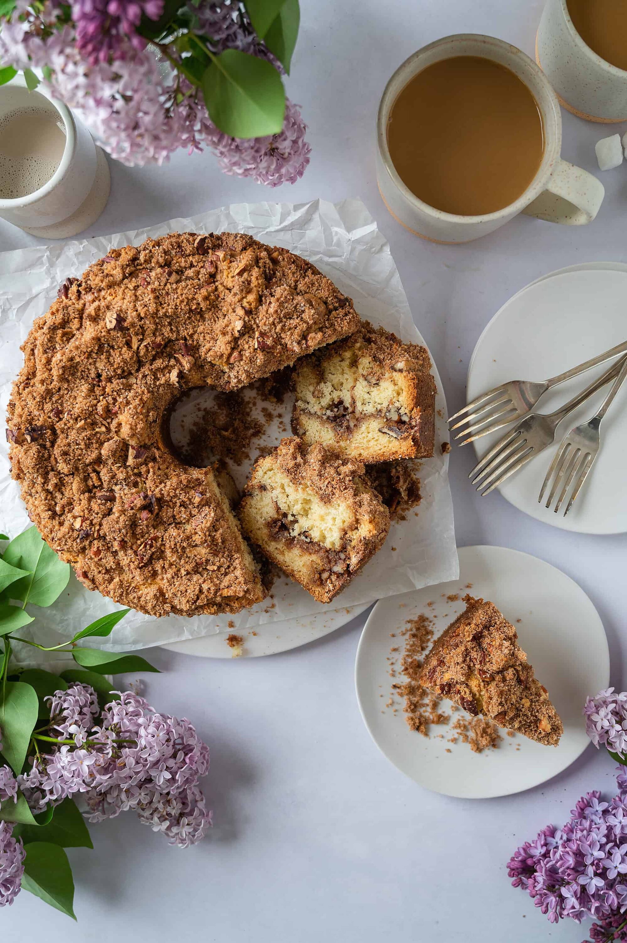 Buttery coffee cake with crumb topping, served with coffee and flowers, perfect for breakfast or brunch.