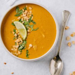 Creamy butternut squash soup garnished with chopped peanuts, cilantro, and a lime wedge. Healthy and comforting winter recipe.
