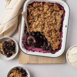 Blueberry crumble dessert in a baking dish with fresh berries and oatmeal topping.