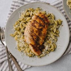Grilled chicken breast with pasta and cheese on a white plate, served with herbs.