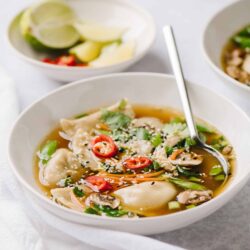 Savory dumpling soup with fresh vegetables and chili slices in a white bowl.