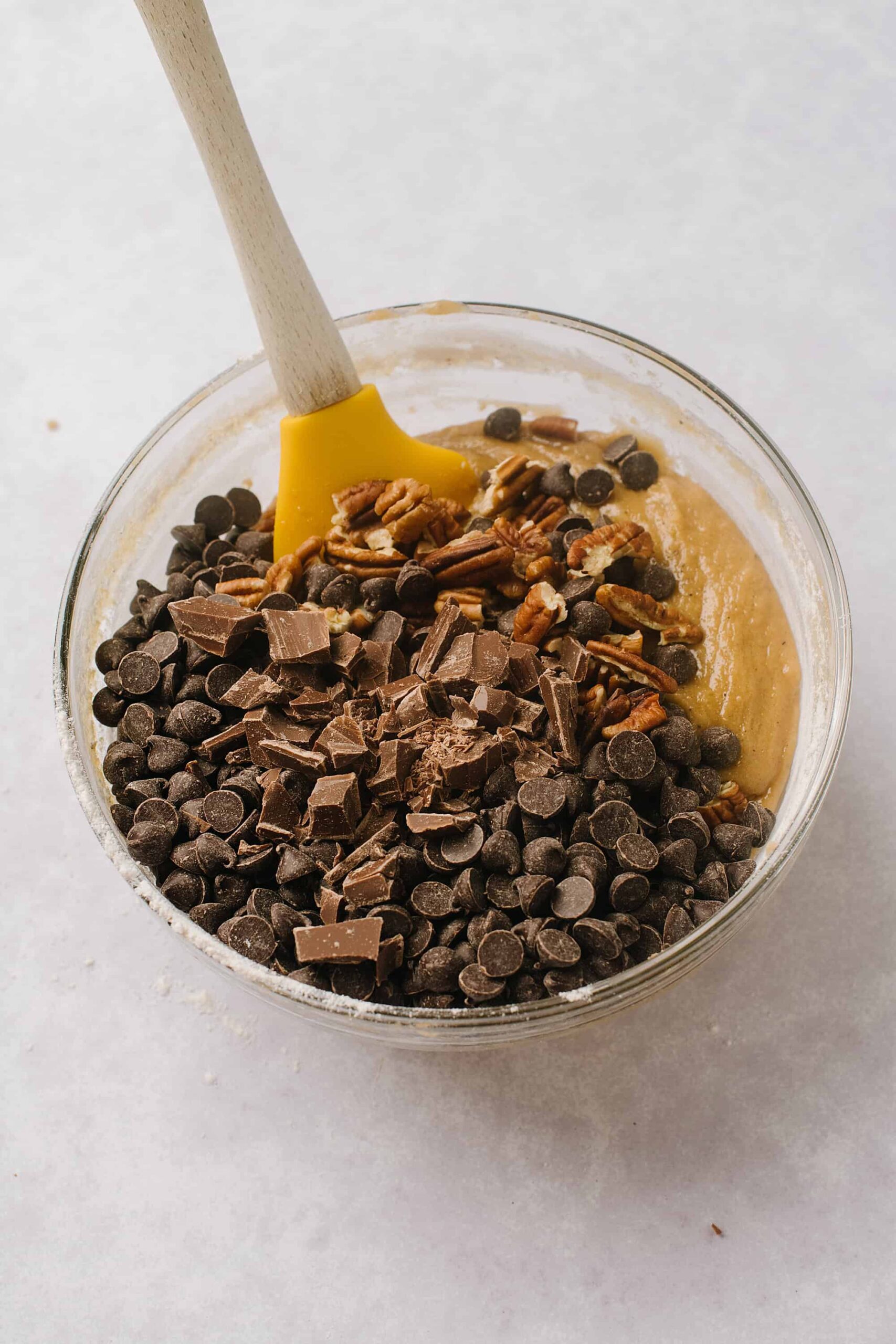 Chocolate chip cookie dough with chopped chocolate and pecans in a glass bowl.
