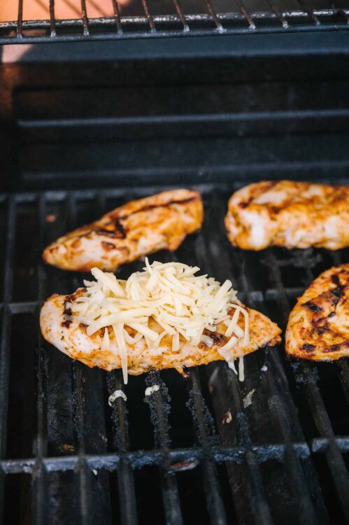 Grilled chicken topped with shredded cheese sizzling on barbecue grill.