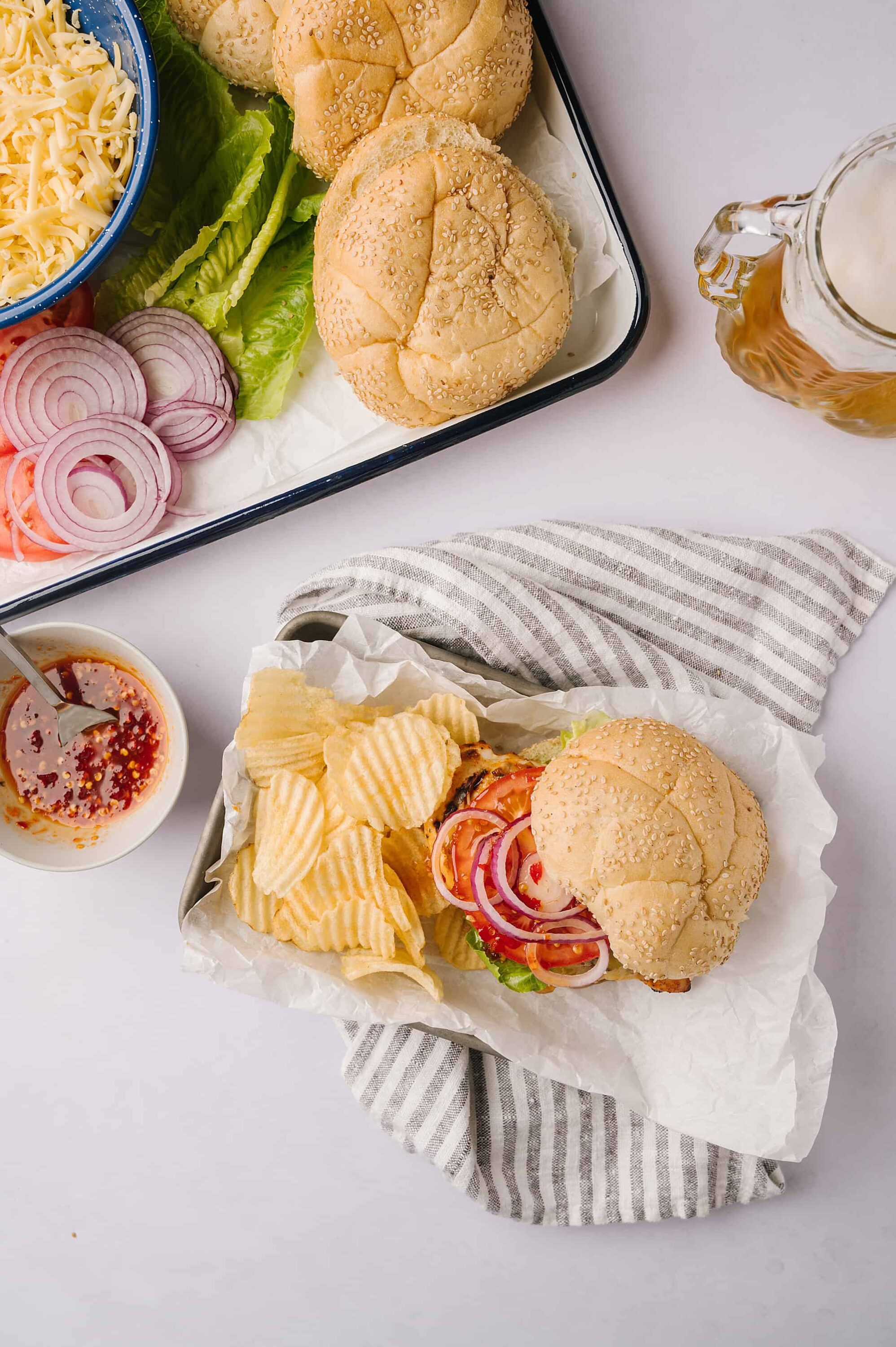 Fresh homemade cheeseburgers with side of potato chips, onions, lettuce, tomato, and condiments. Perfect for quick lunch or casual dinner.