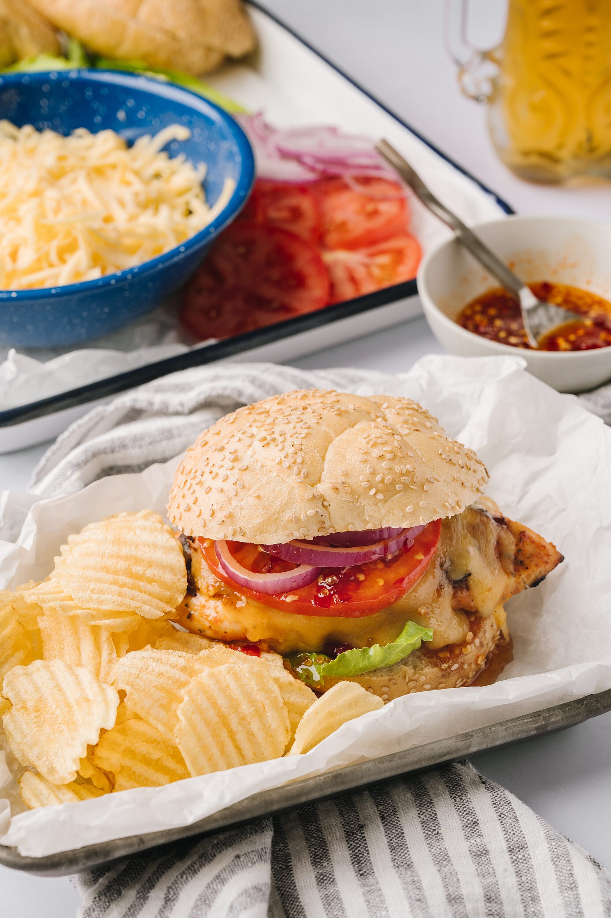 Juicy cheeseburger with fresh vegetables and potato chips on baking tray.